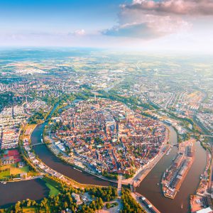 Weite Luftaufnahme einer Stadt mit einem historischen Zentrum auf einer Flussinsel, umgeben von grünen Parks und modernen Wohngebieten.